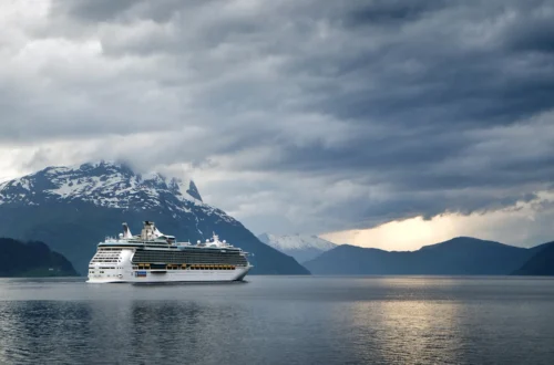 Cruise ship sailing through a Norwegian fjord beneath green mountains on a cool summer day