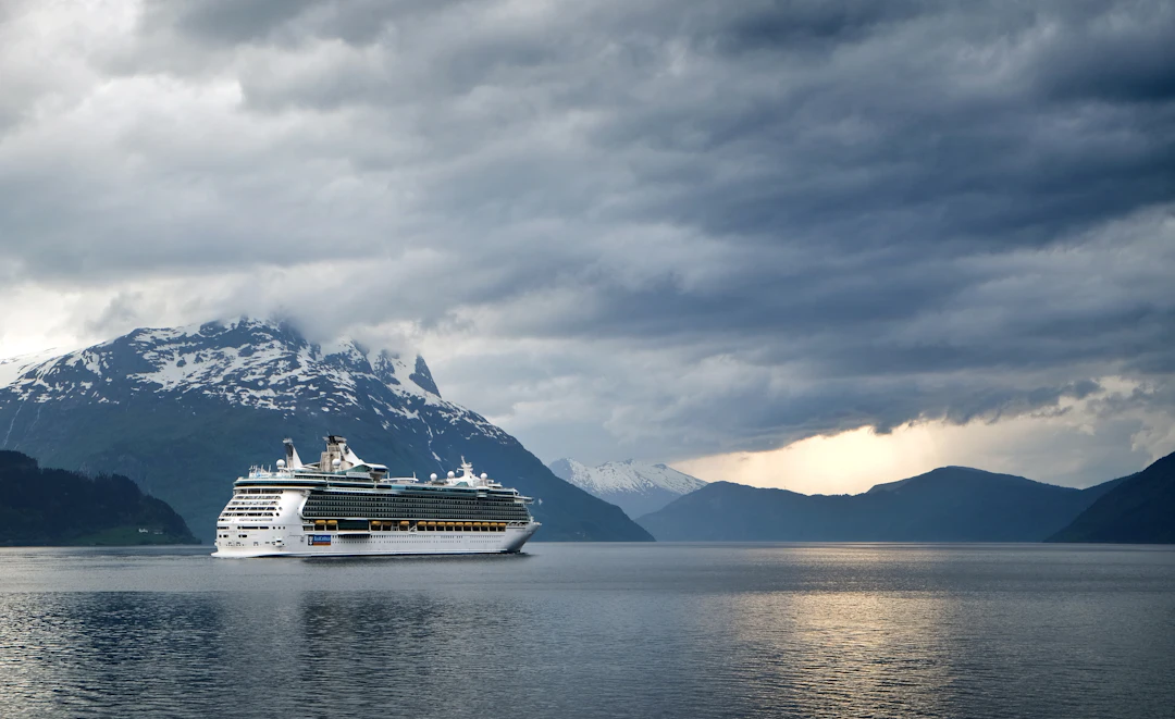Cruise ship sailing through a Norwegian fjord beneath green mountains on a cool summer day