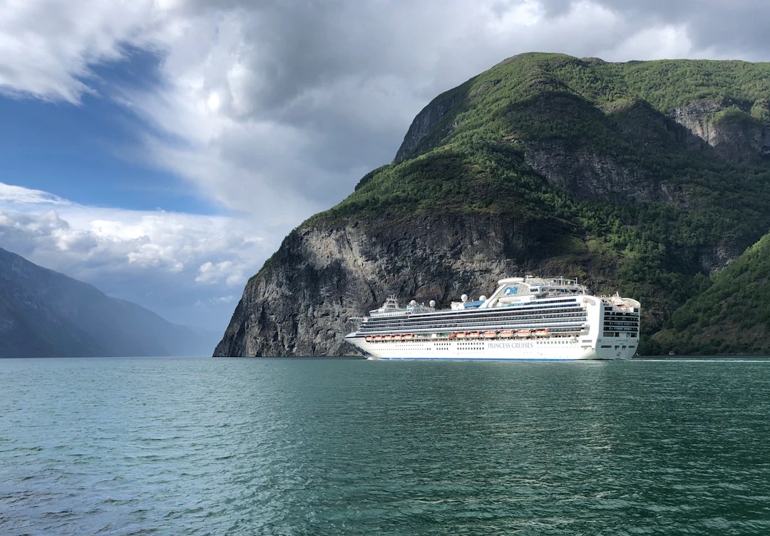 Large cruise ship sailing between steep rocky mountains on deep green water in Norway